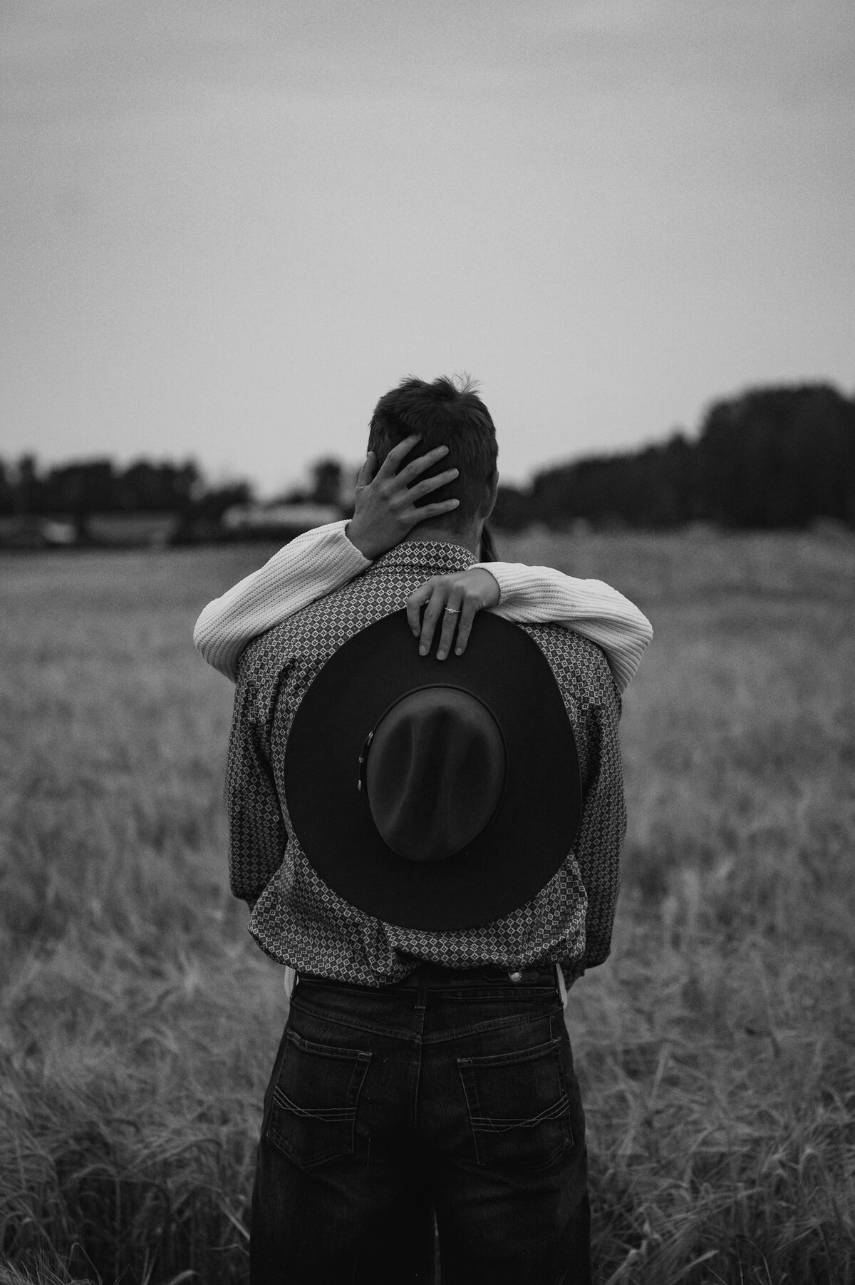 Black and white engagement photo of girl holding cowboy hat and showing off her ring in Alberta