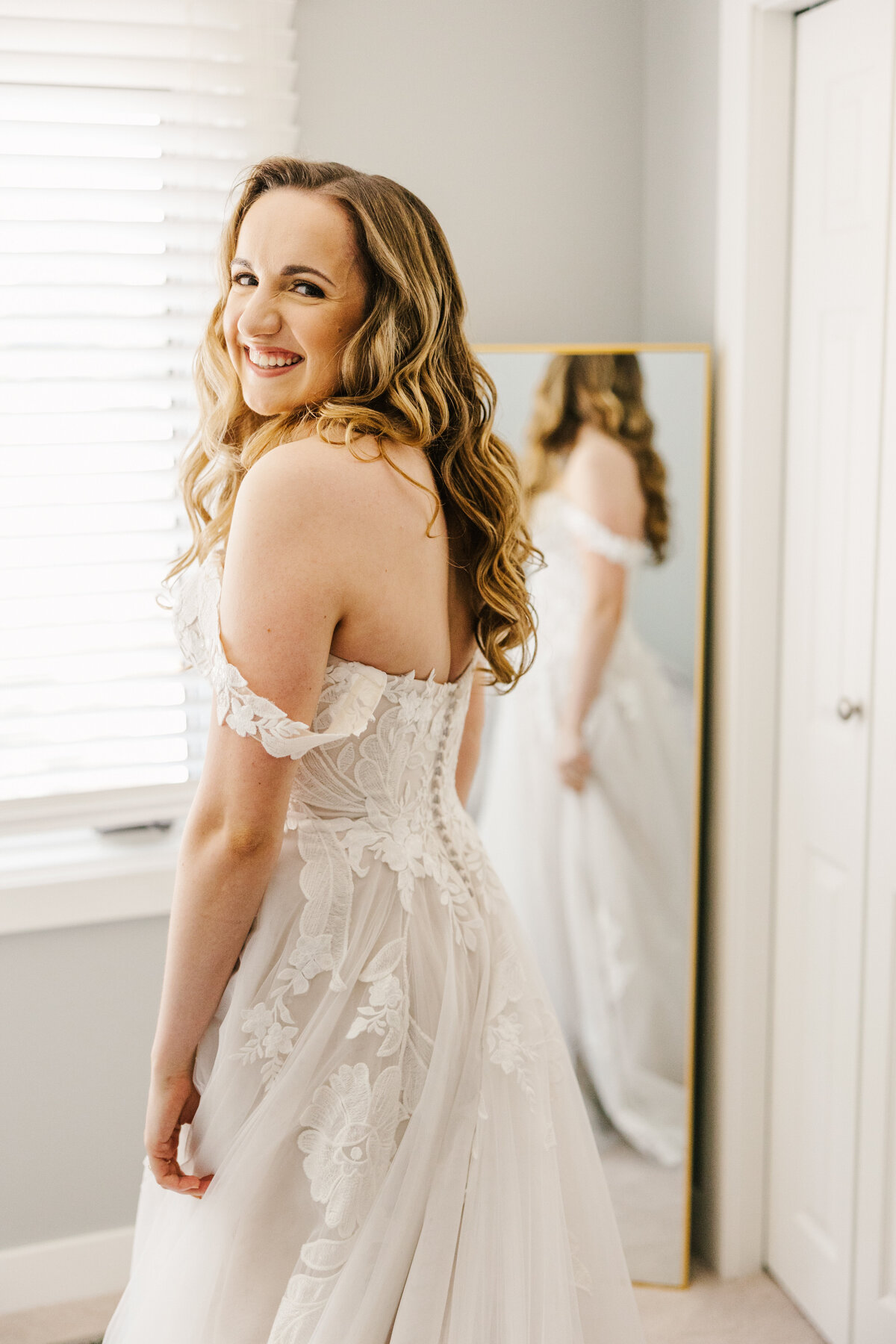 Bride smiling over her shoulder while standing in front of a mirror