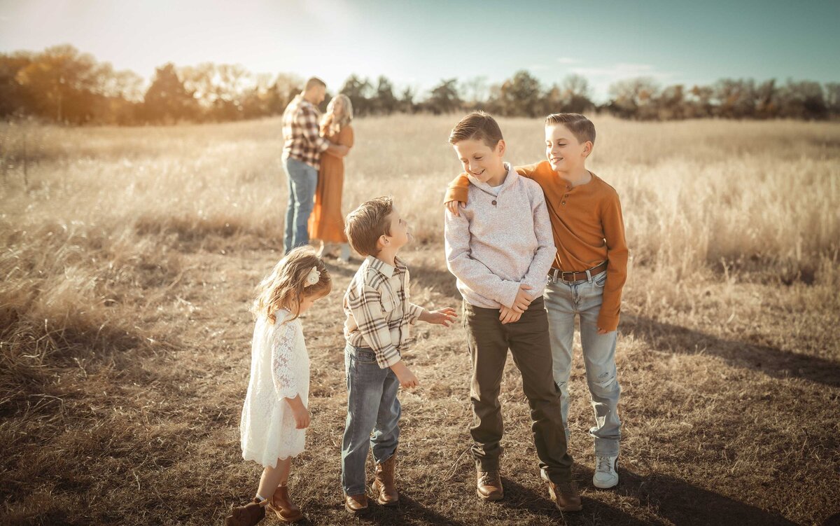 A family of seven having a fun at their  photo session. Brothers and sister are standing in front of their parents. the parents are in the background holding each other and smiling