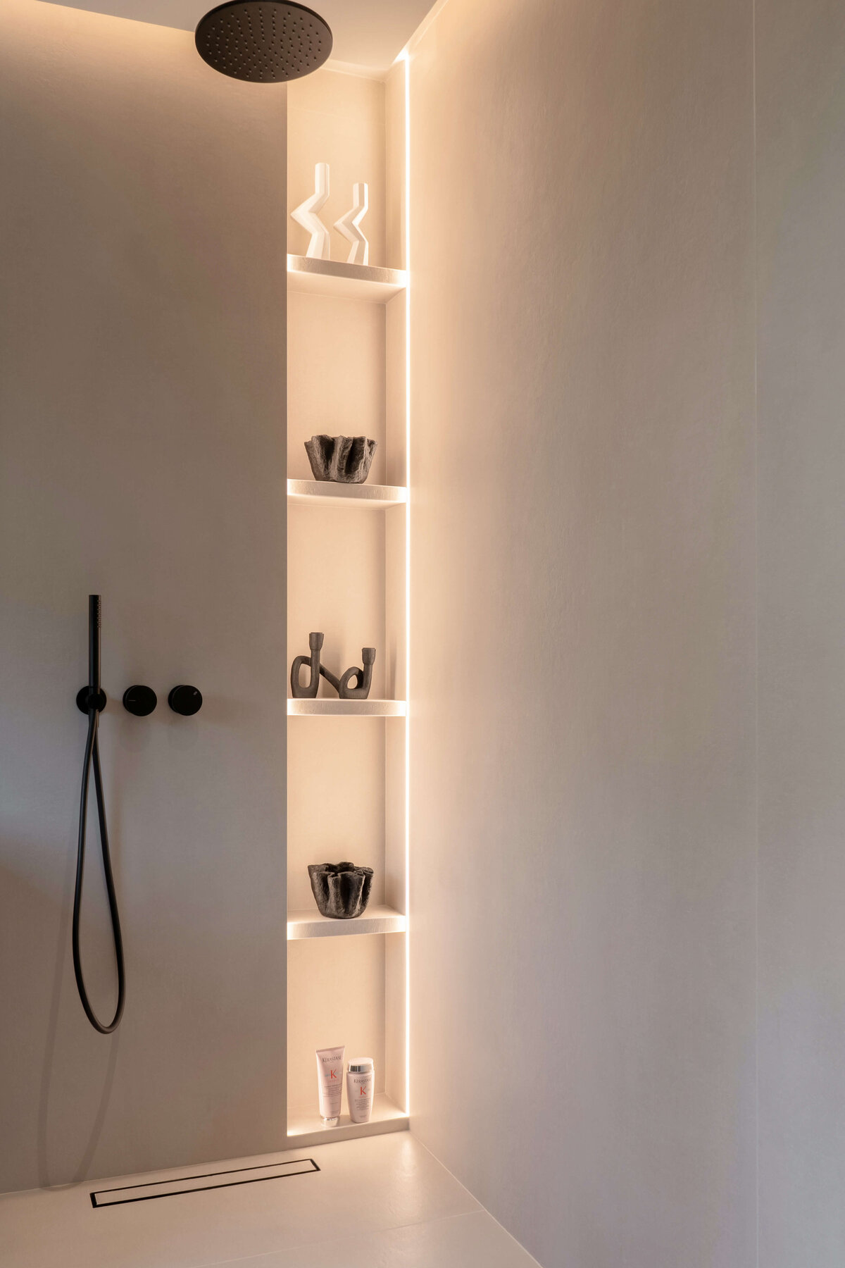 Sleek neutral walk-in shower that has built-in shelves emitting a soft, warm light. The shower hardware is start black, adding a dramatic edge to the shower.