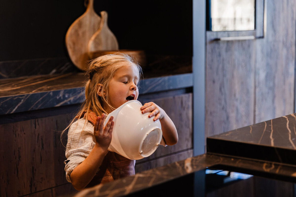 meisje staat in keuken en likt uit de kom waar beslag in is gemaakt