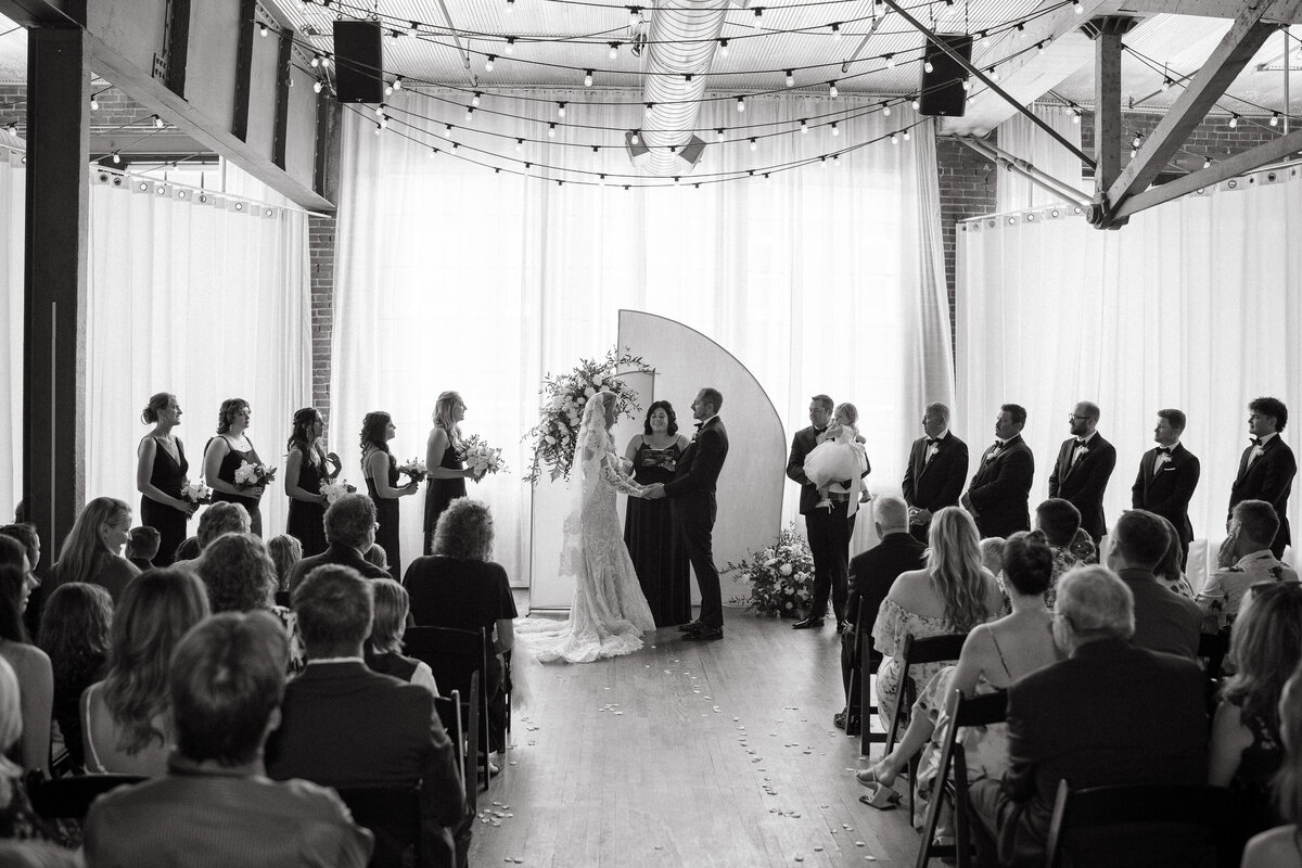 A bride and groom standing up at the wedding ceremony in front of family and friends