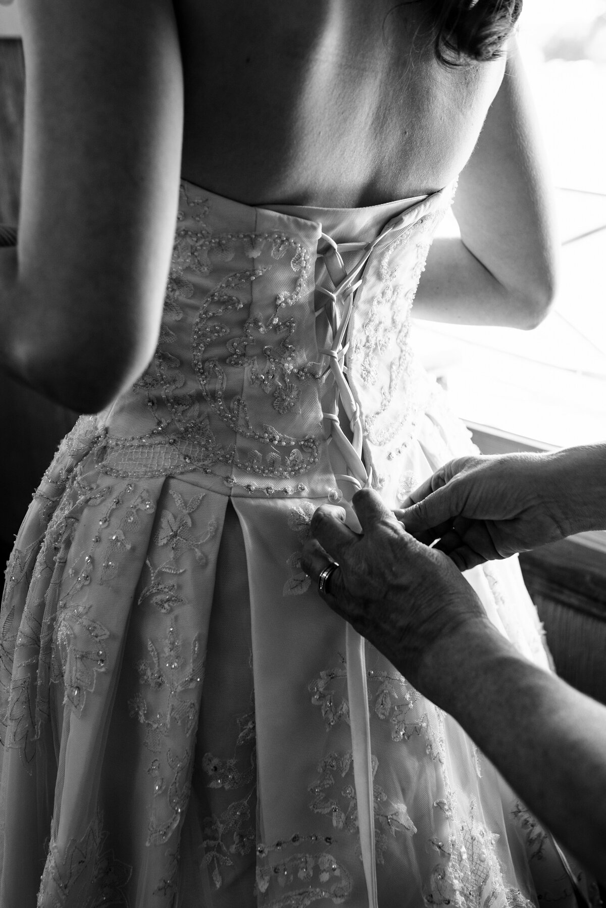 Black and white up close photograph of a mom tying the corset of her daughter's wedding dress by Charlotte wedding photographers DeLong Photography