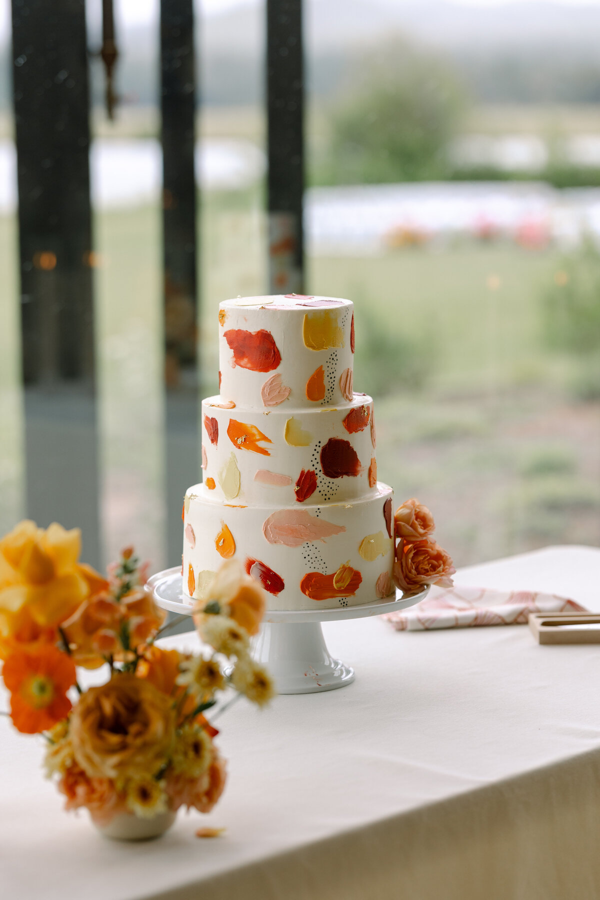 Tired white wedding cake with splashes of bold and vibrant orange, pink, peach and yellow on a cake table representing full service calligraphy and design by Life in Letters