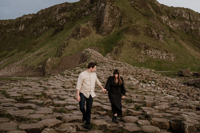 Séance photo de couple en irlande, sur les roches noires de la Chaussée des Géants avec un couple marchant main dans la main.