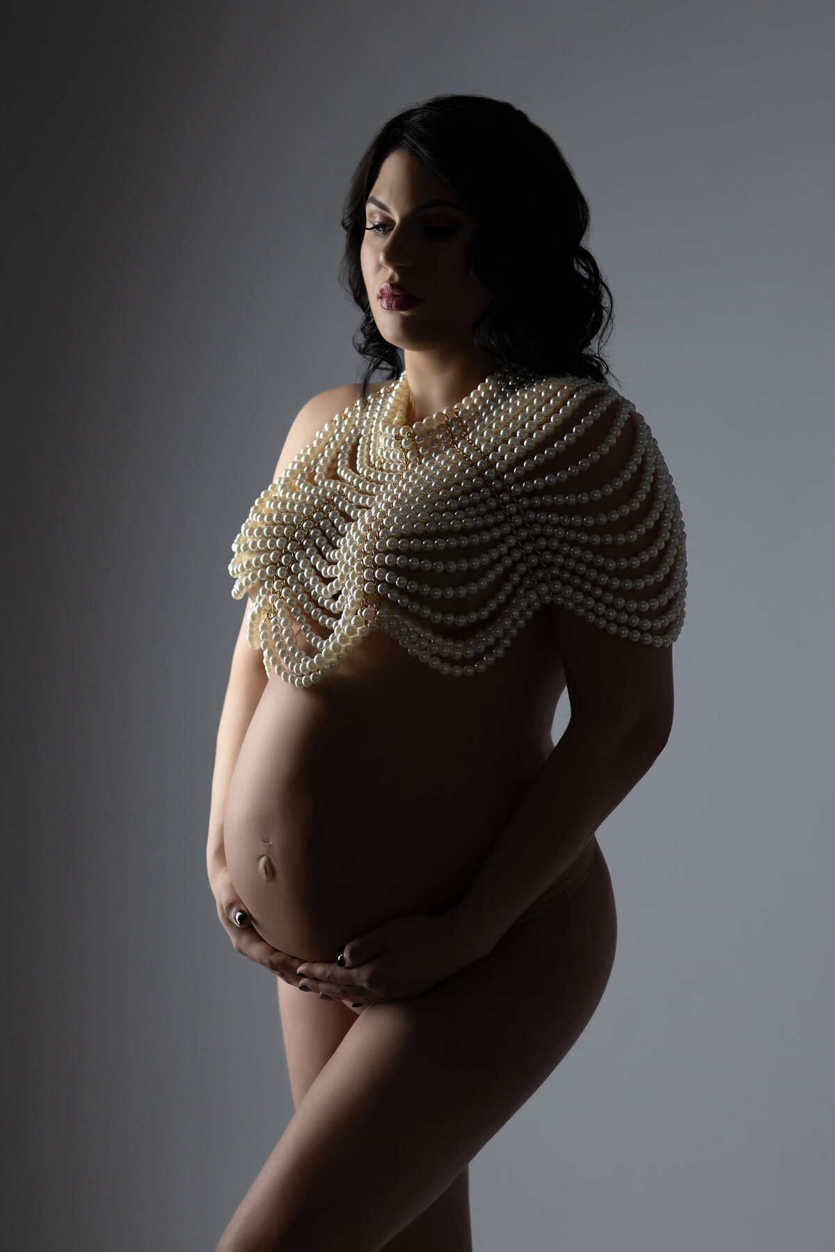 Maternity photography in Dallas featuring woman adorned in pearls against a soft, moody backdrop.