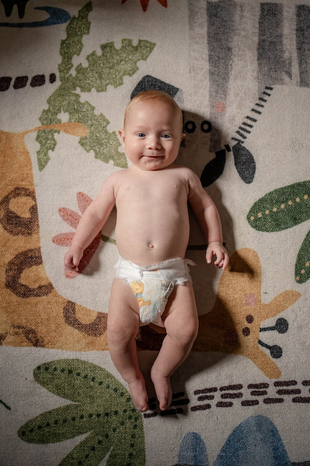 Baby just in diaper on jungle rug in nursery