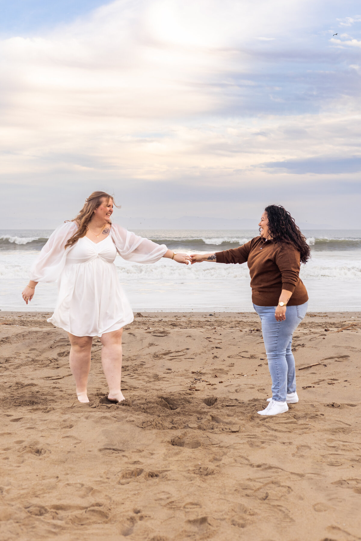 a masc femme lesbian couple dance at their beach engagement photoshoot
