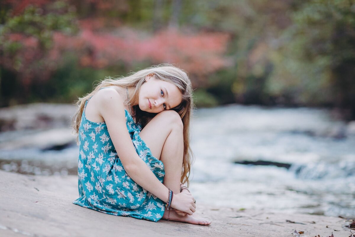 A girl sitting on a rock next to Line Creek in Peachtree City Georgia  with her knees pulled up and her head on her knees.