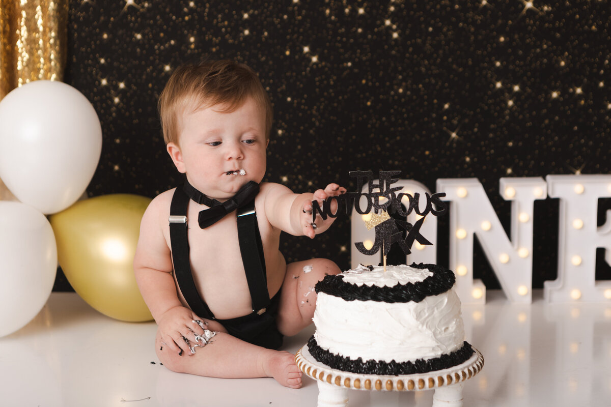 Boy in suspenders and bow tie with black and white cake