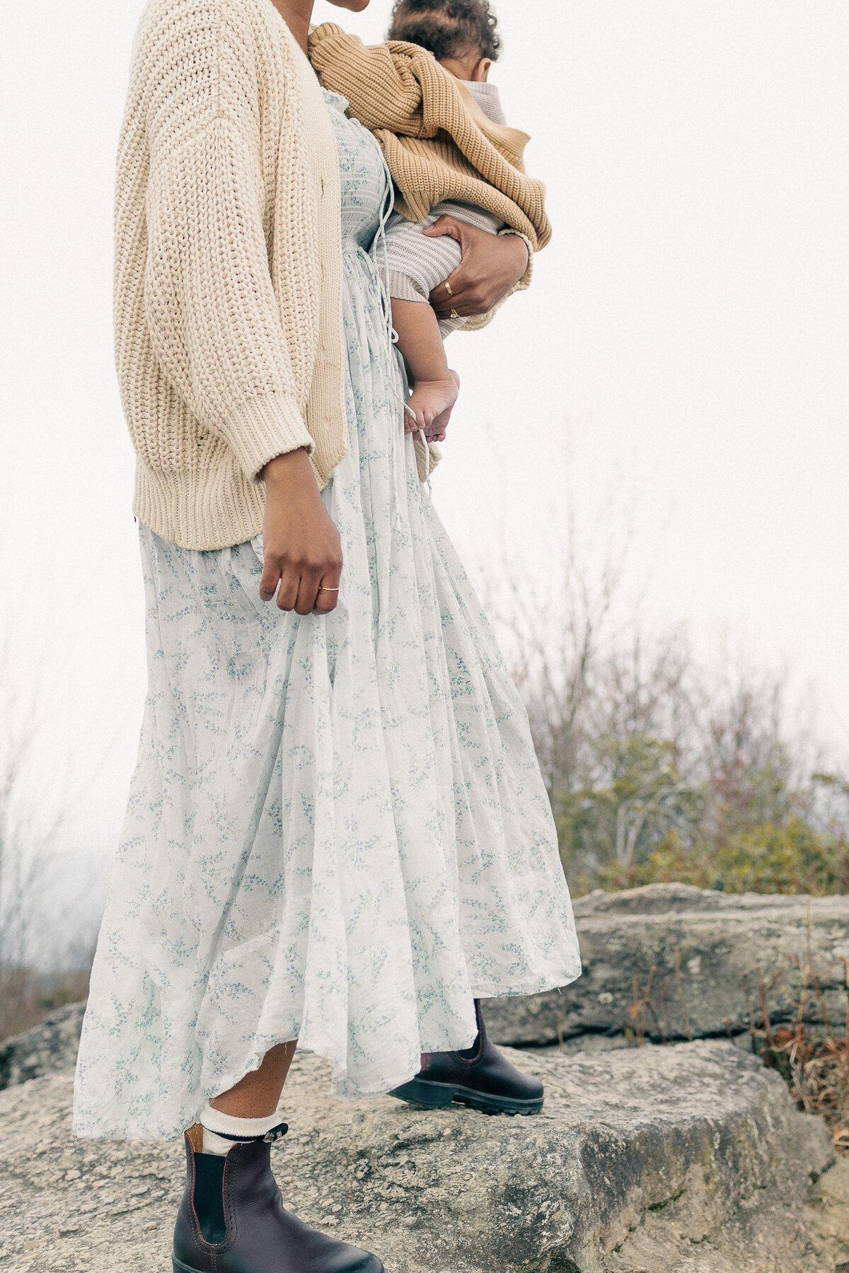 A detail portrait of a mother holding her dress while cradling and swaying her baby on her hip during a Kansas City outdoor newborn session.