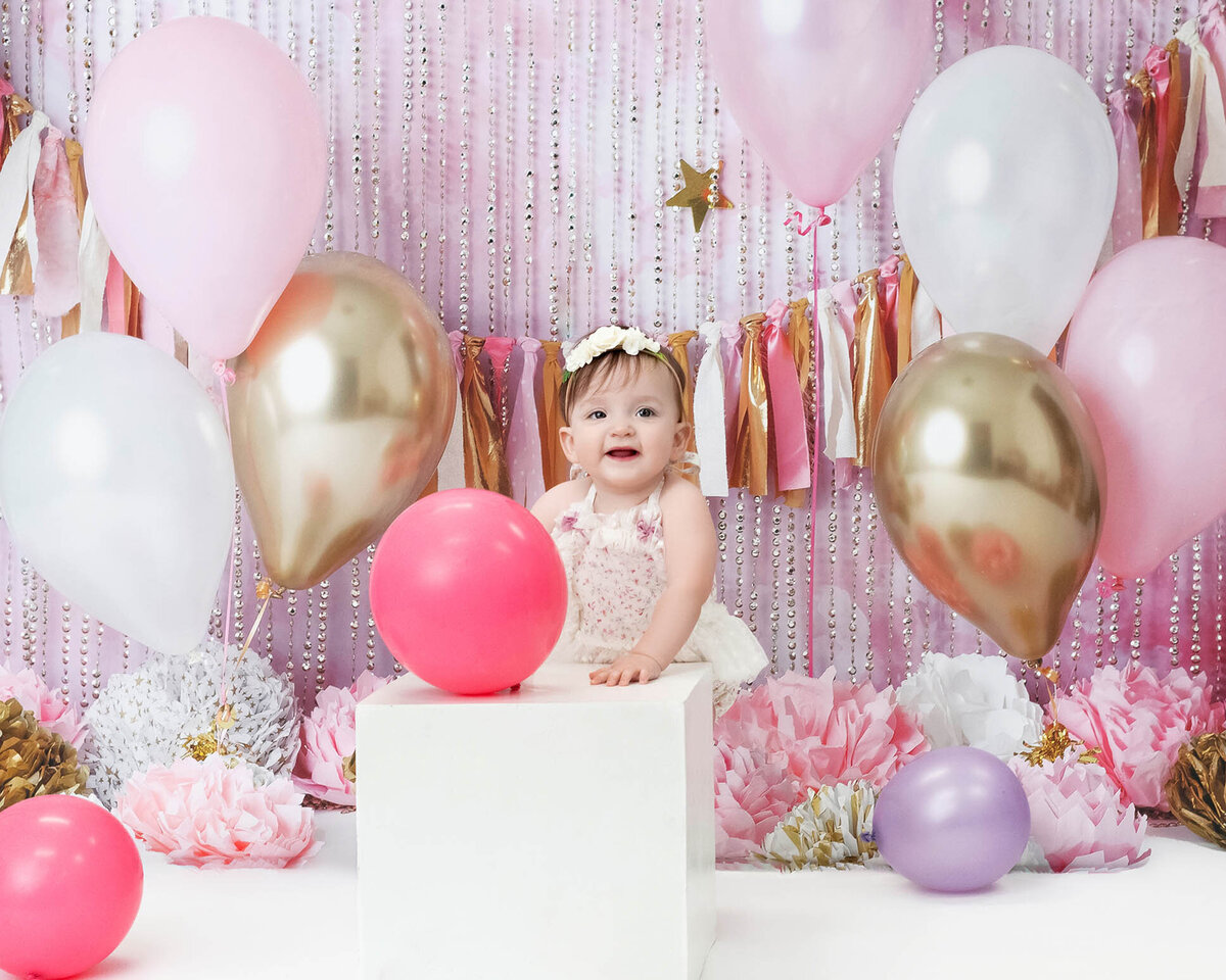 A bay stands against a white box in a pink studio celebrating her bithday