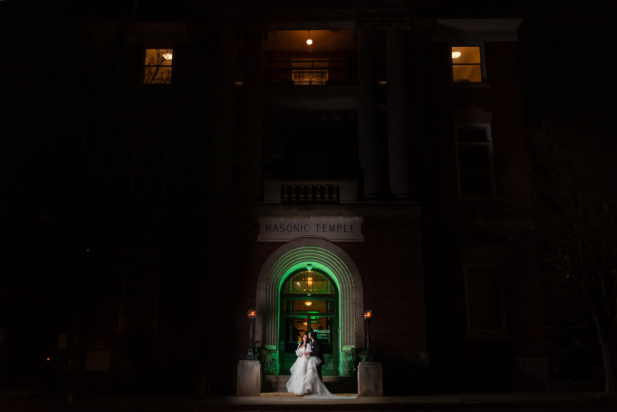 Portrait-of-bride-and-groom-in-front-of-the-Asheville-Masonic-Temple-at-night-with-a-green-arch-lighting-up-the-building-by-Charlotte-wedding-photographers-DeLong-Photography