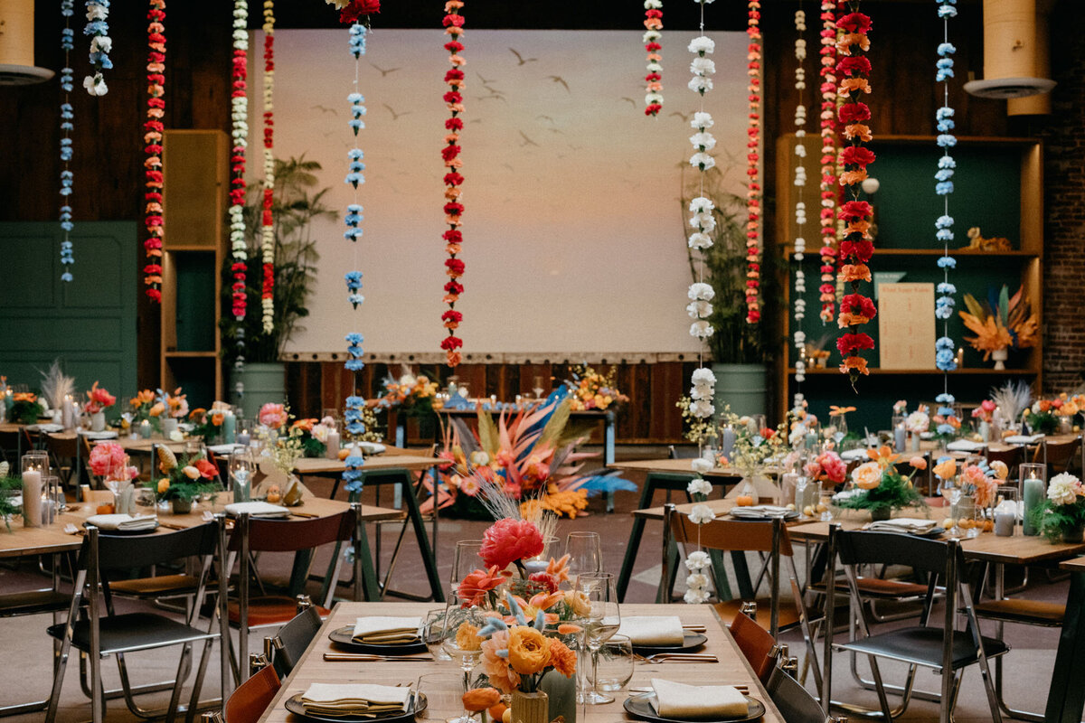 Indoor wedding reception set up with long hanging flower chains, and an overall fun and bright industrial feel.