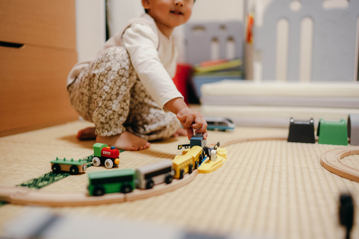 男の子が木製レールの上を電車を走らせて遊んでいるシーンお