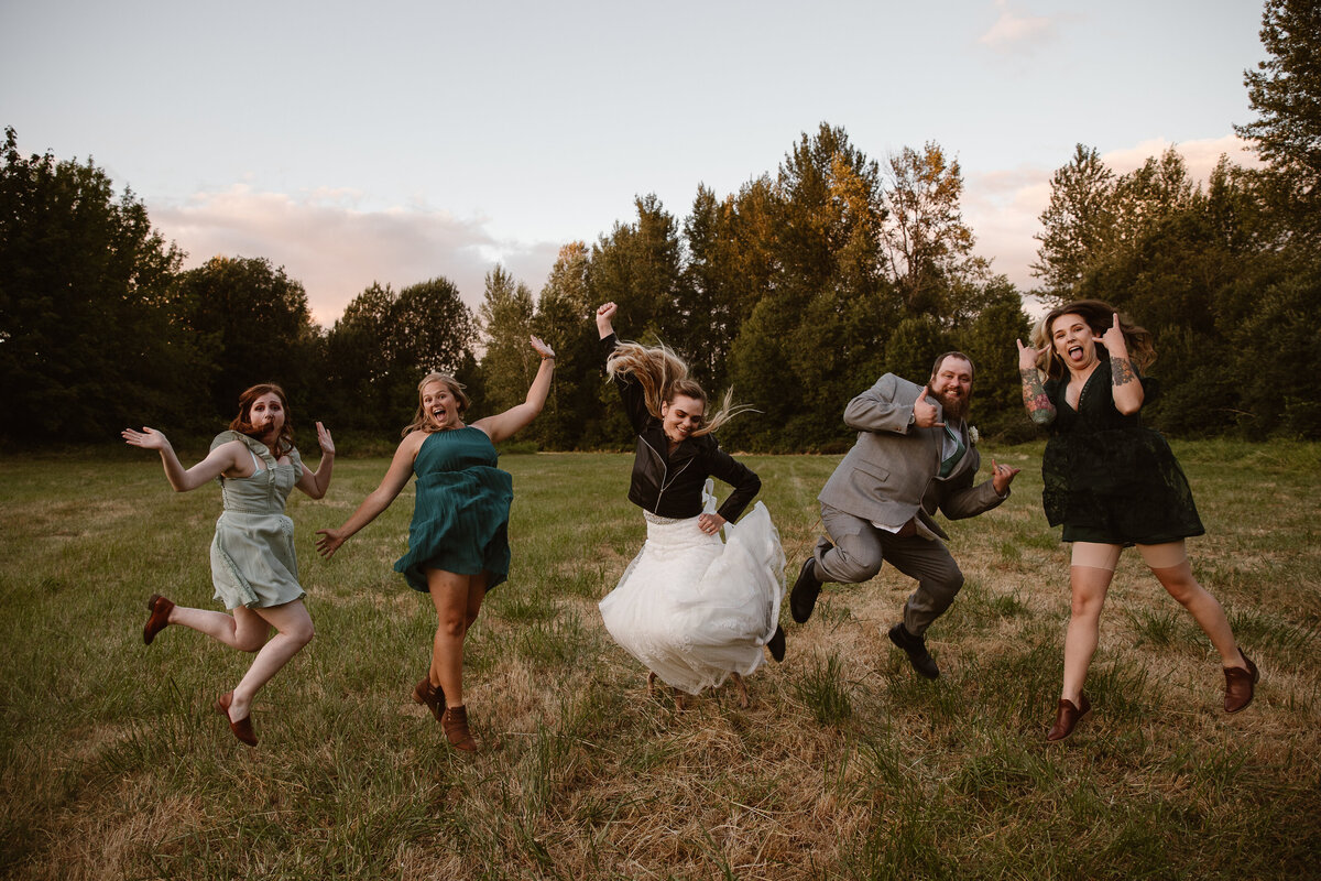 bride, groom, and wedding party jump in the air for a photo in field
