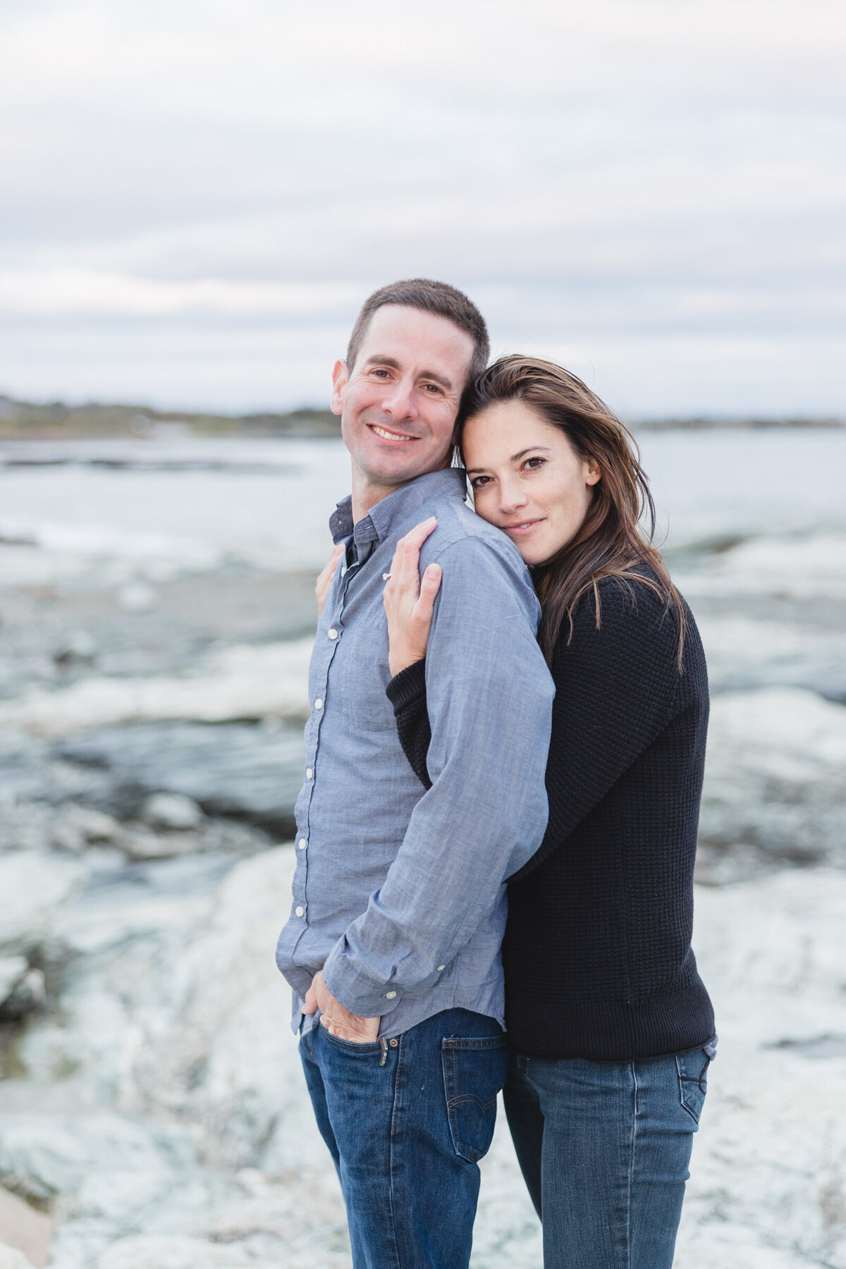 Engaged couple embrace on the coast of Newport