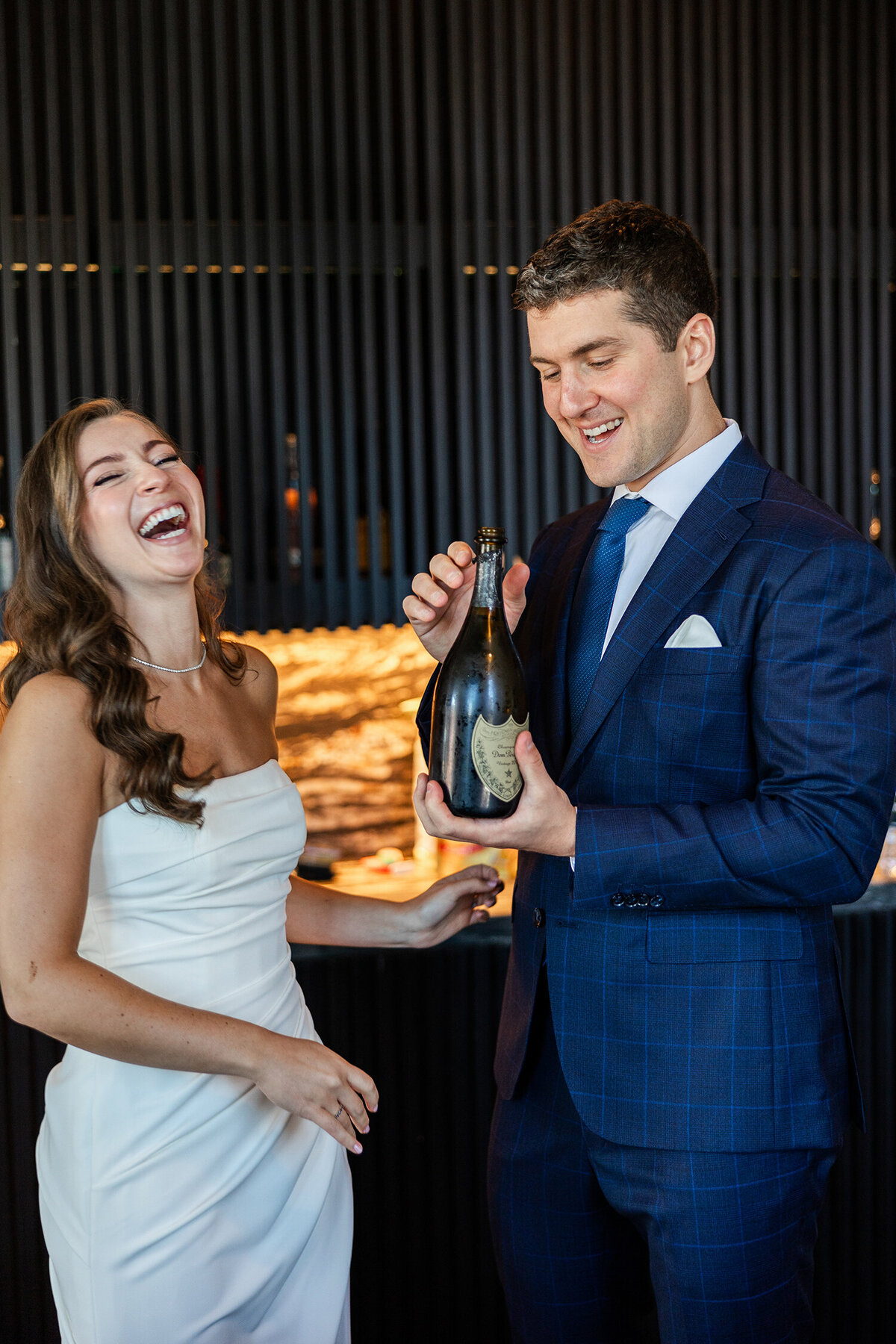 Bride and groom laughing while opening a champagne bottle