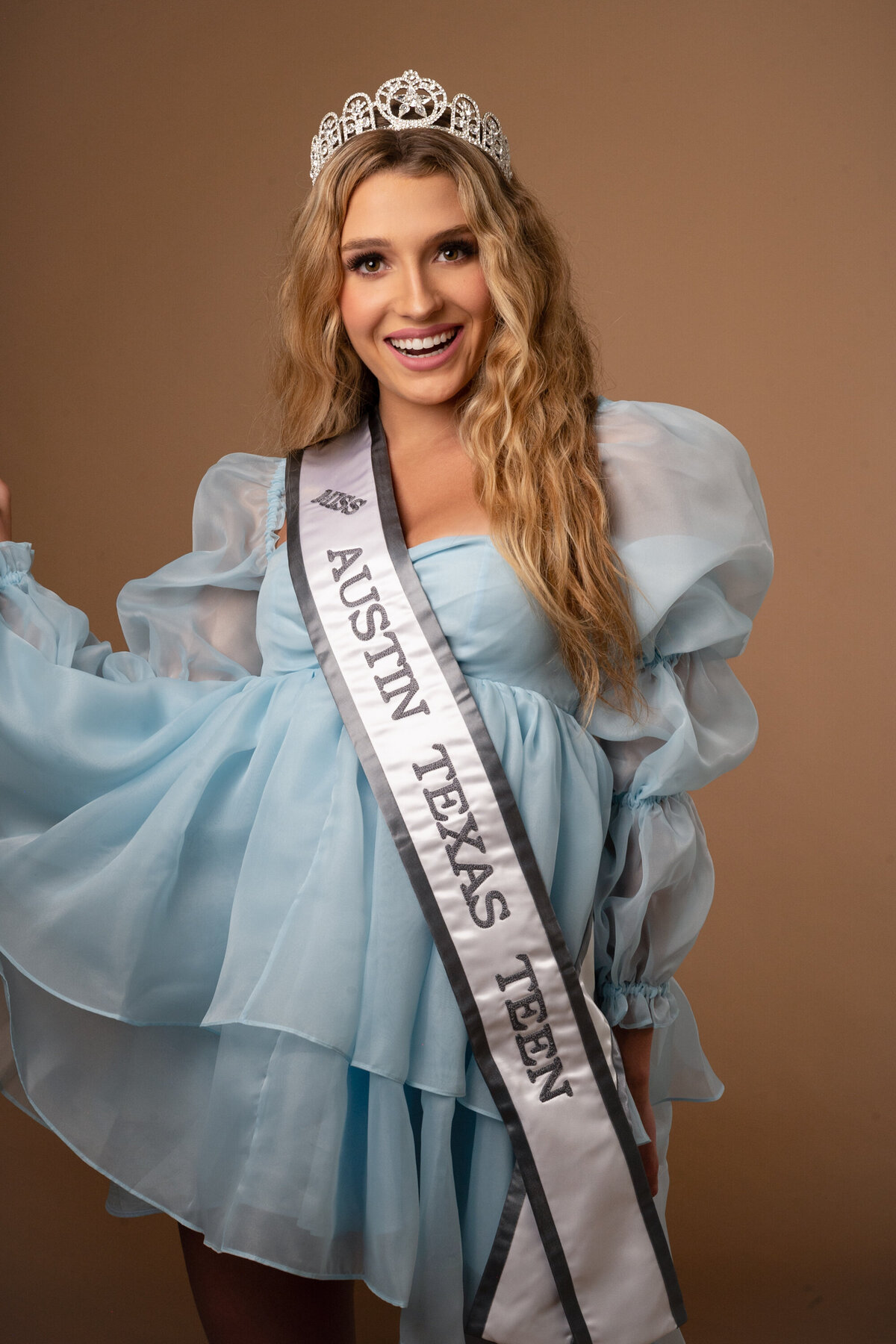 A smiling young woman wearing a sparkling tiara and a sash