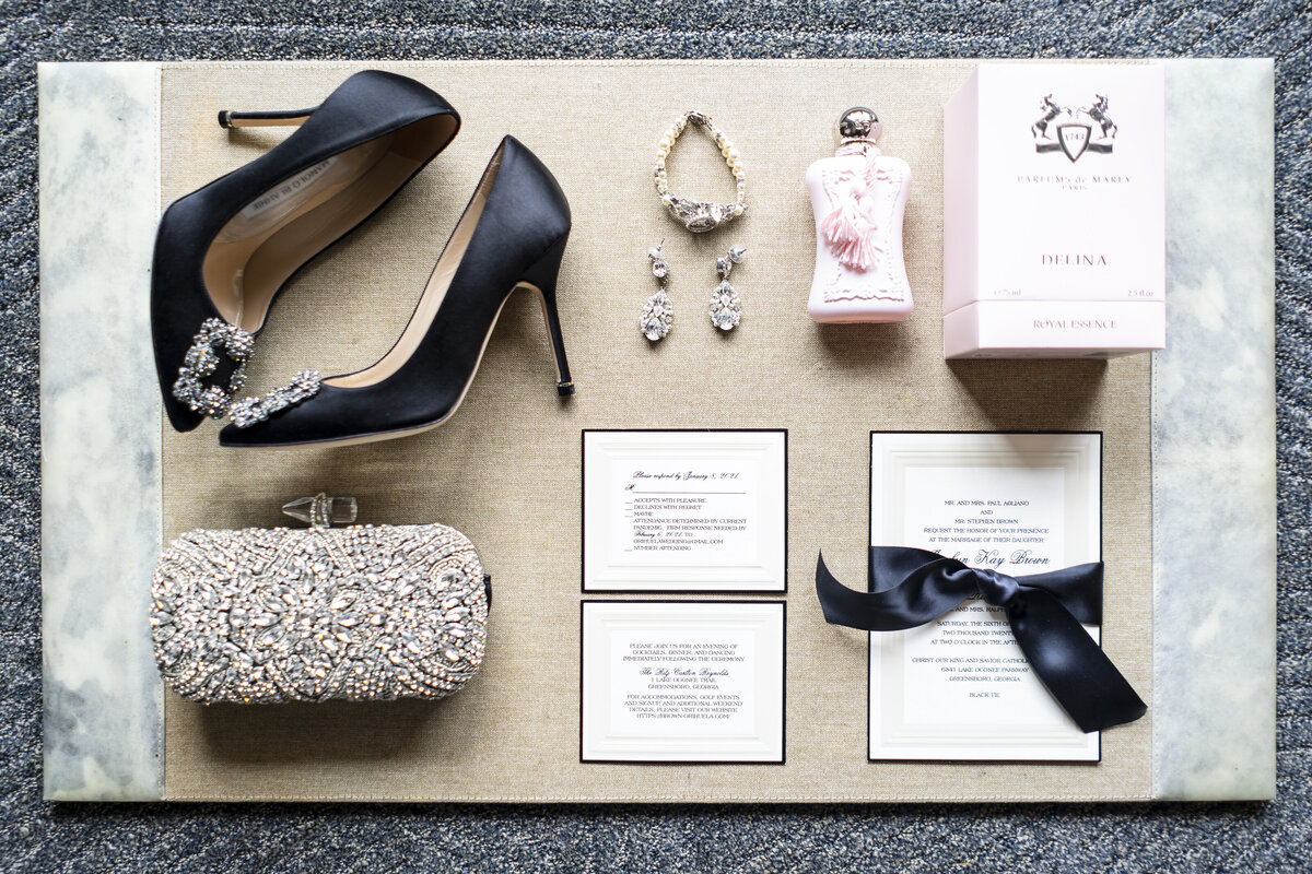 Details from a wedding showing black heels, invitations and a clutch.
