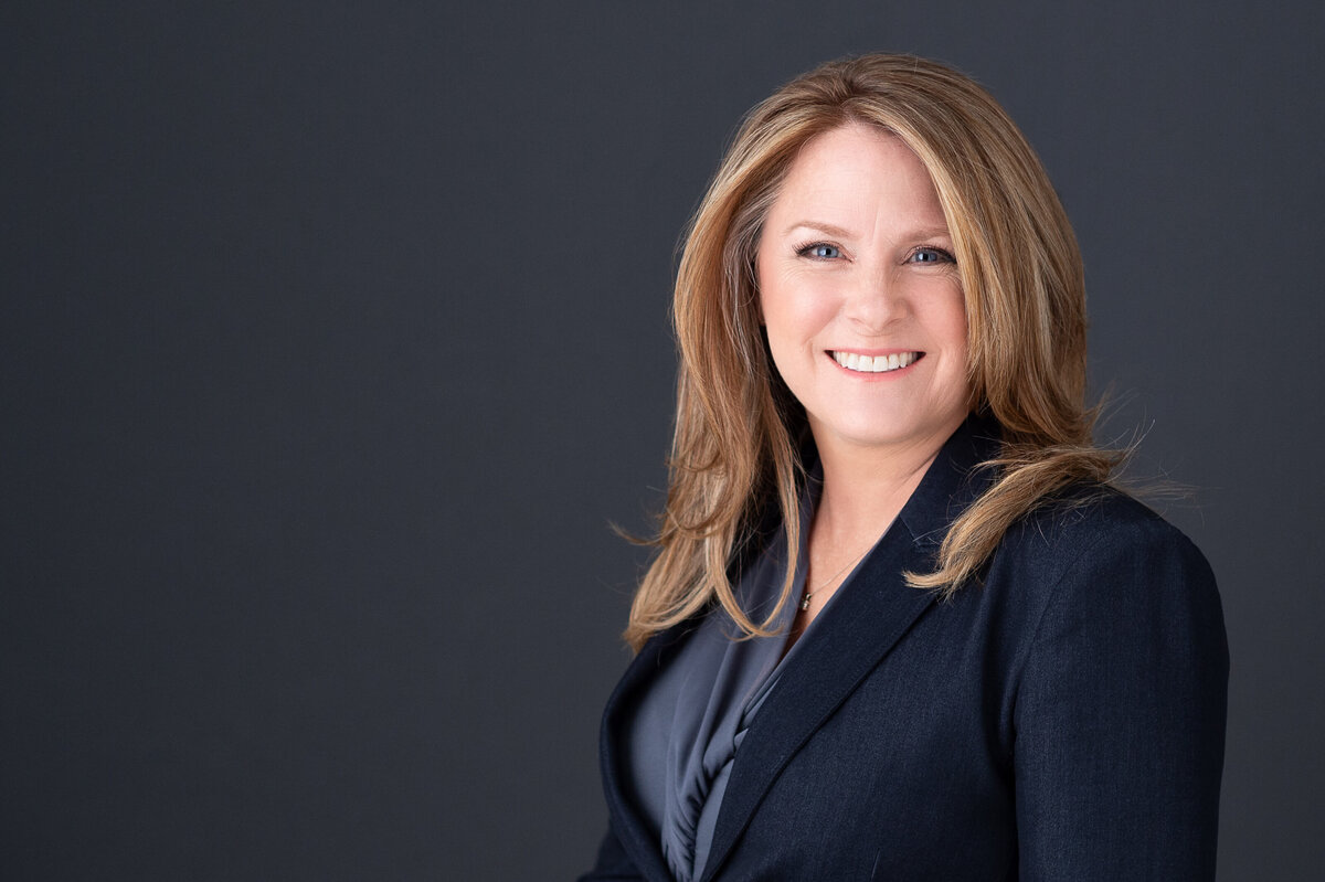 a blonde woman in a navy suit jacket smiling at the camera.  Captured by Ottawa headshot photographer JEMMAN Photography