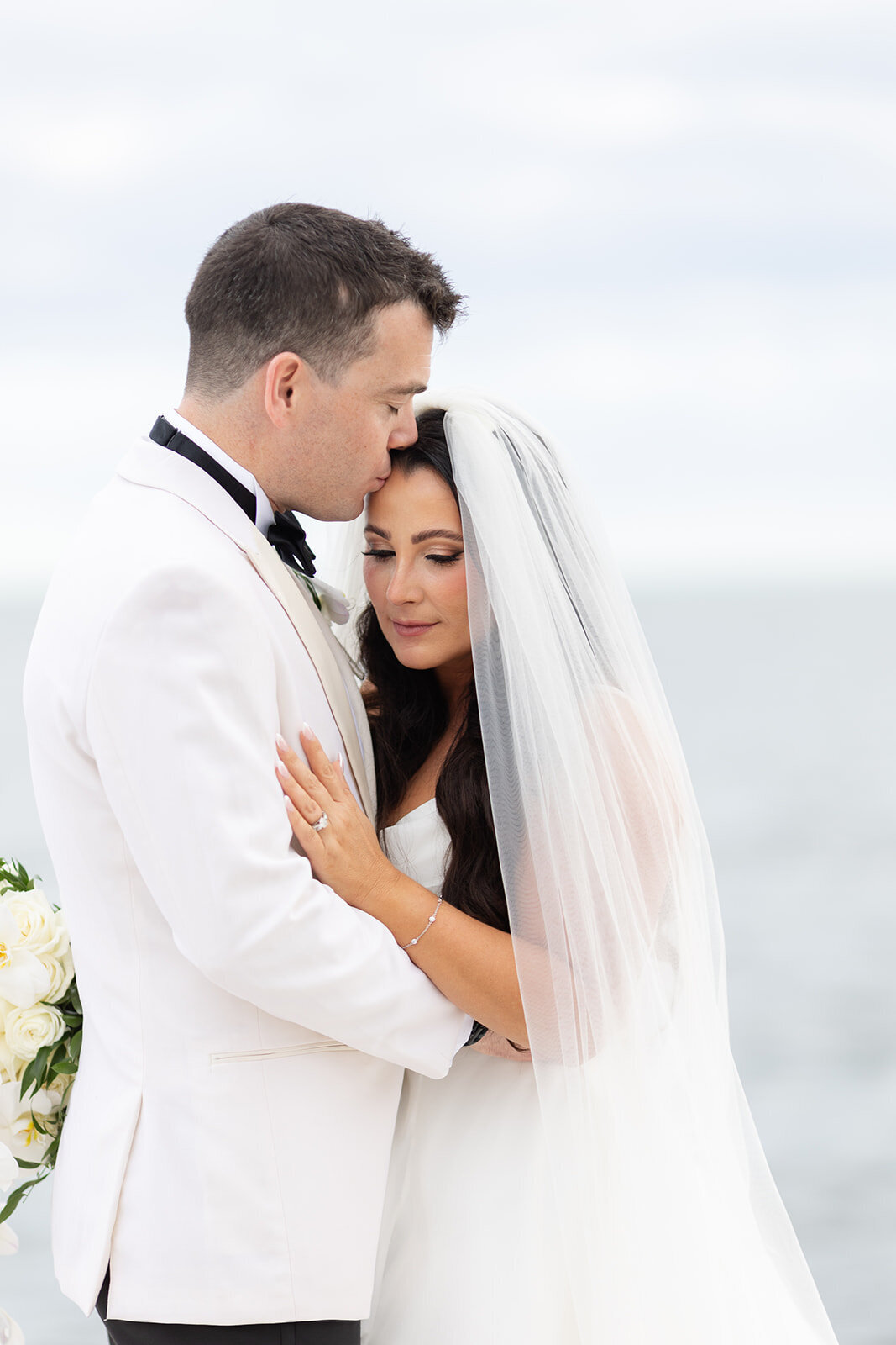 Bride and groom share an intimate embrace by the ocean, with the groom kissing the bride’s forehead during their Miami wedding, photographed by Claudia Amalia Photography.