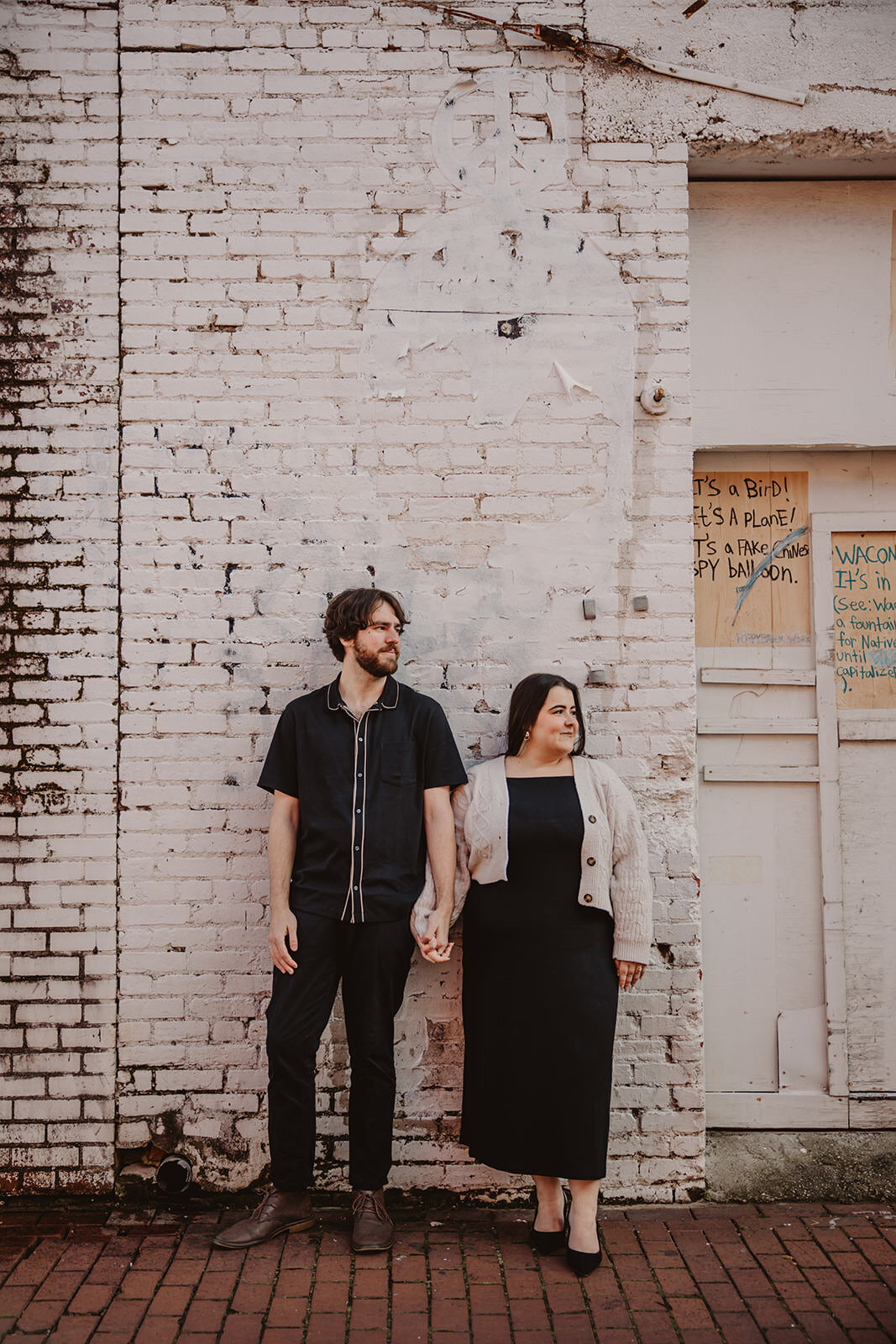 A couple holding hands and standing in front of a white brick building 