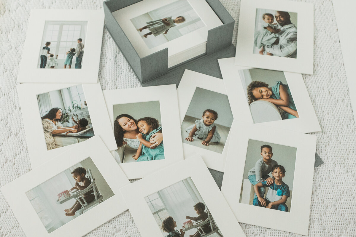 Gray linen box full of matted photos sits on a blanket surrounded by more scattered family