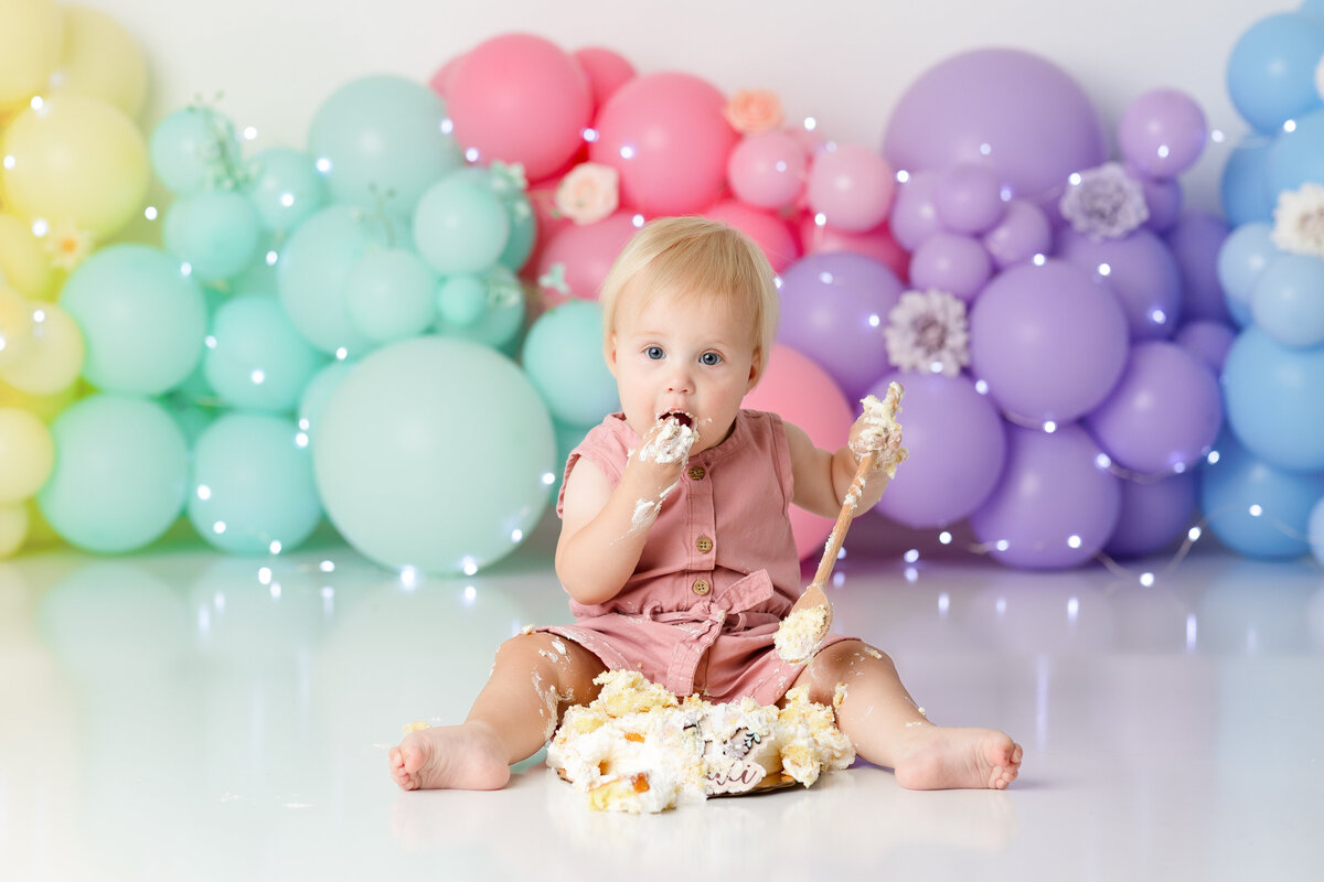 One year old Tampa baby enjoying a personalized luxury cake smash session with colorful rainbow decorations