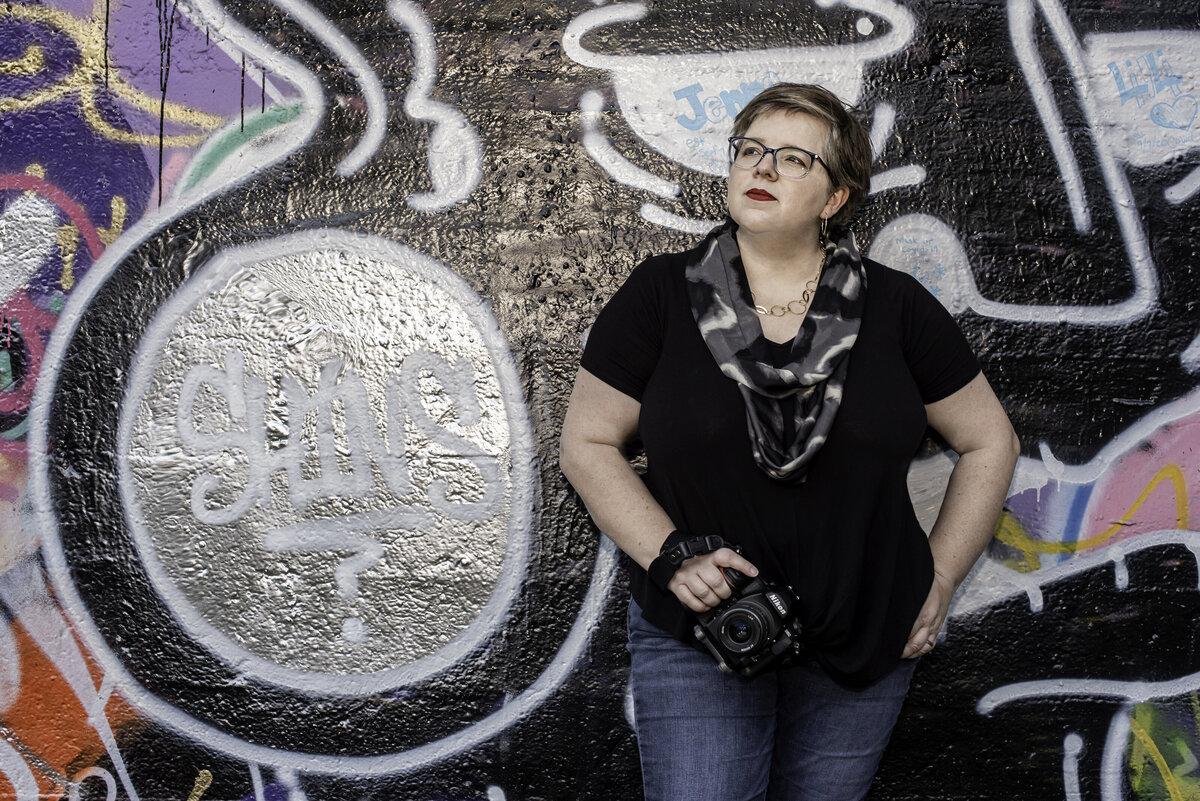 photographer posing with camera in front of graffiti wall