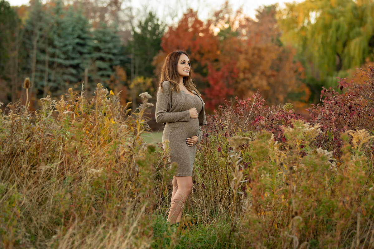 pregnant woman wearing a beige dress in field with fall foliage for her outdoor fall maternity session in Burlington, ON
