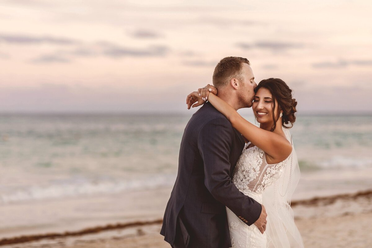 Groom kissing bride on side of face on beach at Secrets Maroma Riviera Maya