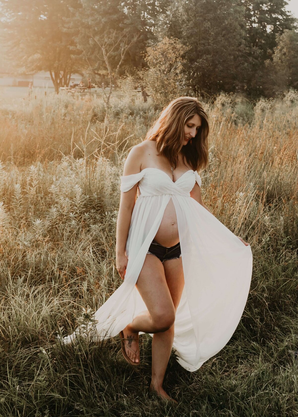 A pregnant woman in a white dress standing in a field captured by a Pittsburgh maternity photographer.