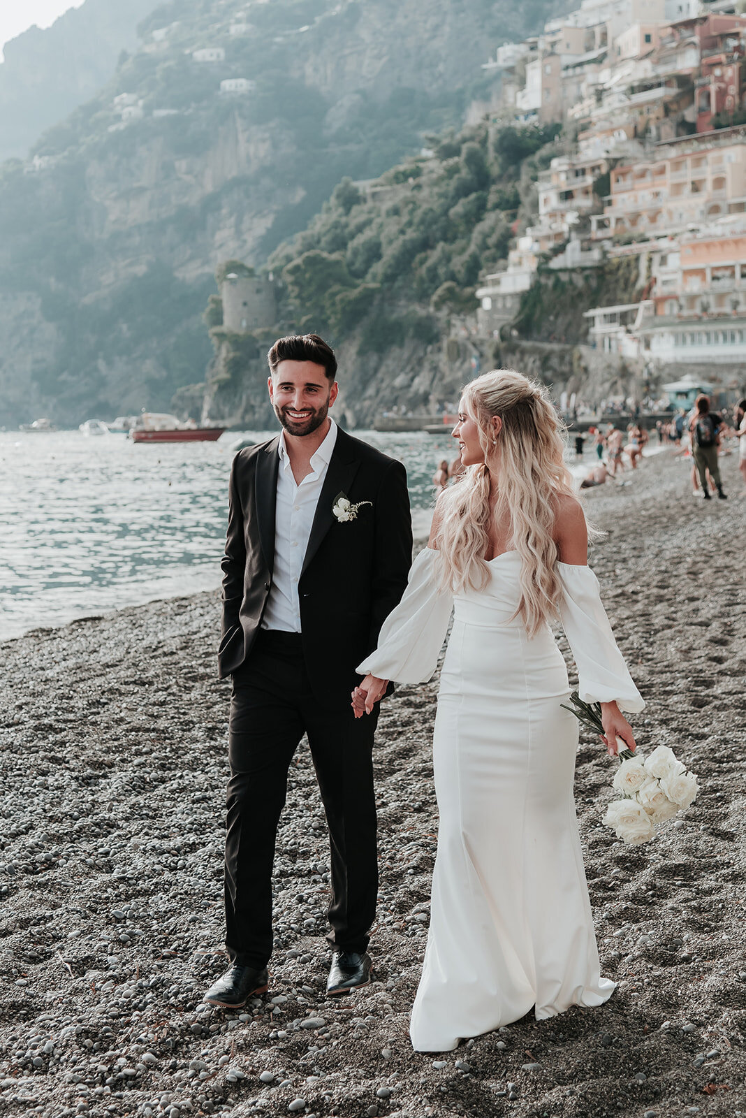 Bride and Groom walking hand in hand along the stone beach in Positano