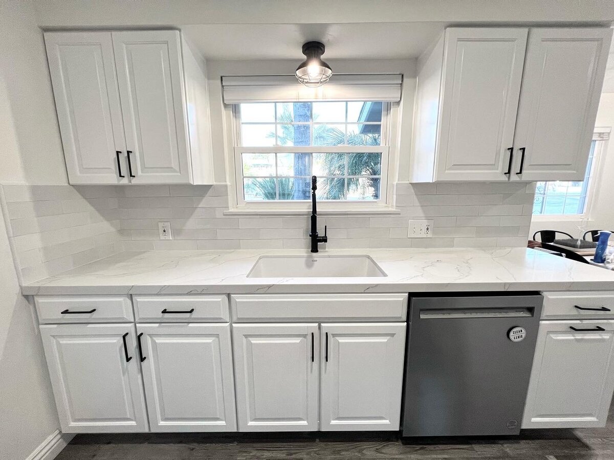 A remodeled kitchen with white cabinets and white countertops and black hardware