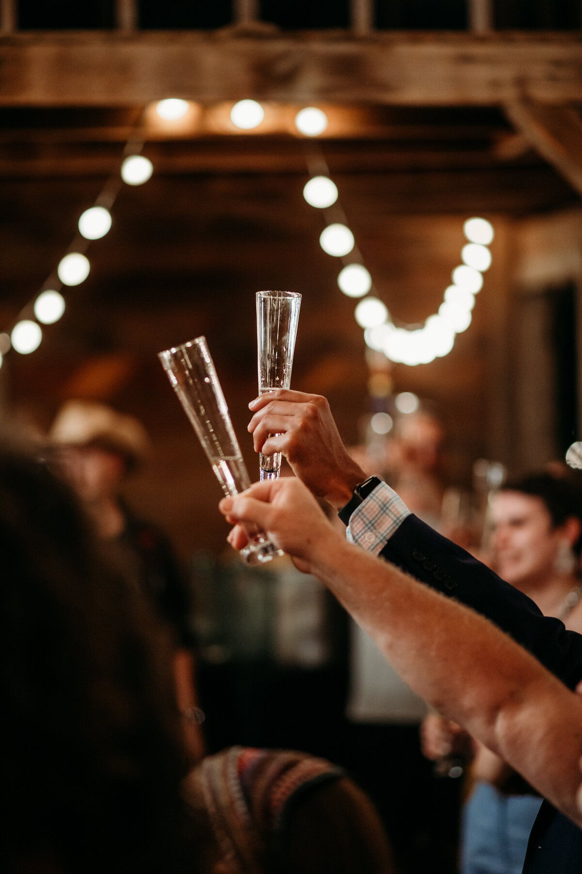 Two hands holding champagne flutes aloft for a toast, with a blurred background of a festive gathering