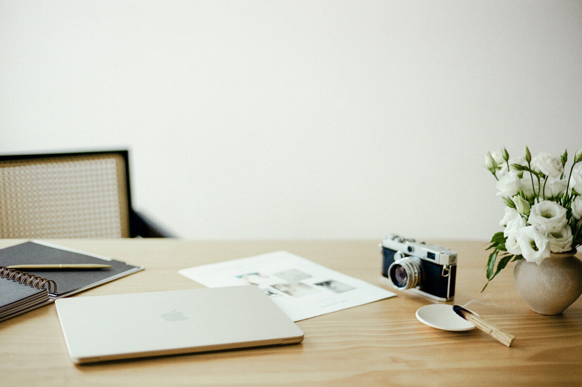 horizontal branding photo of desk with vintage camera, closed macbook, warm tones