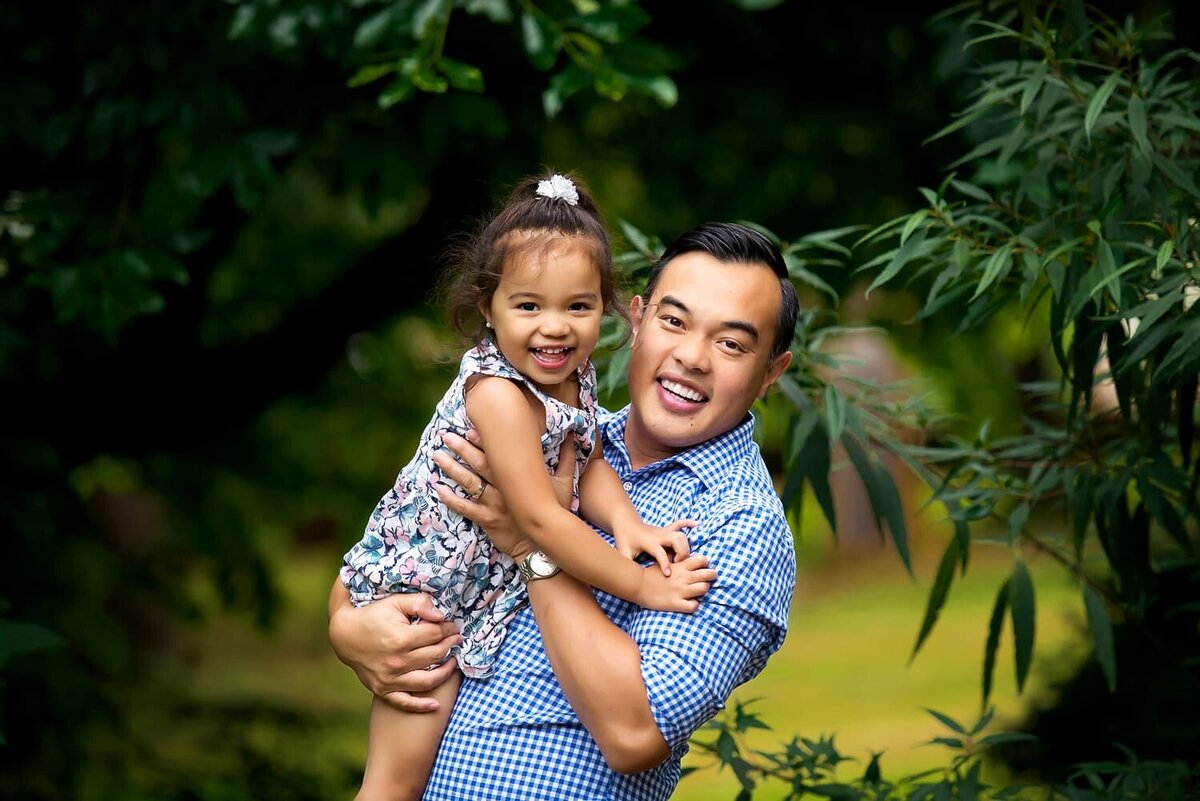 Father and toddler daughter laughing during family photoshoot at Queens Park in New Westminster