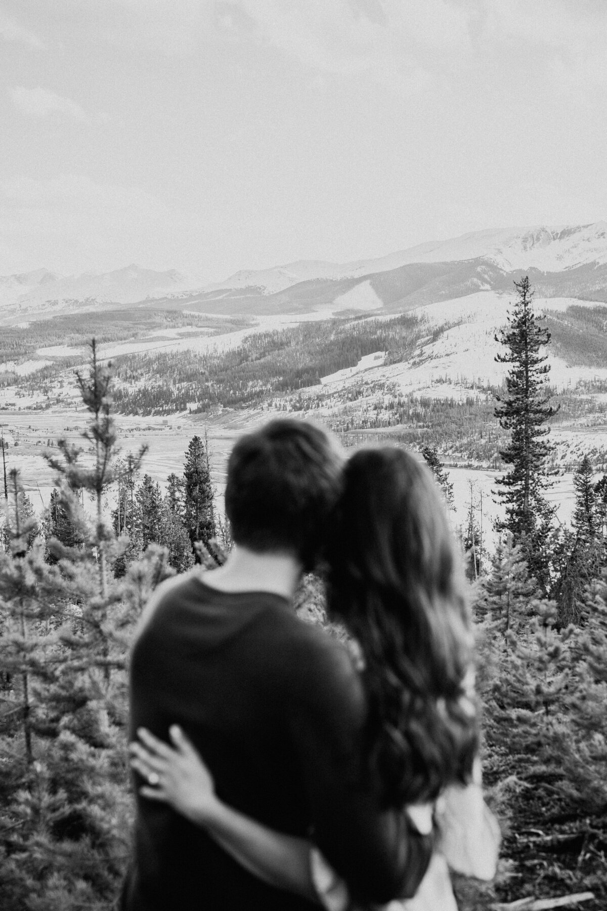 Couple embraces while overlooking the snowy valley from a mountaintop in Sapphire Point.