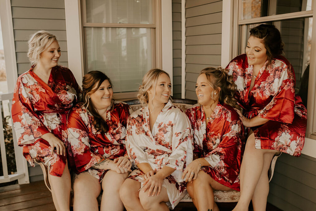 bride and bridesmaids sit on the porch of the farmhouse in their getting ready robes