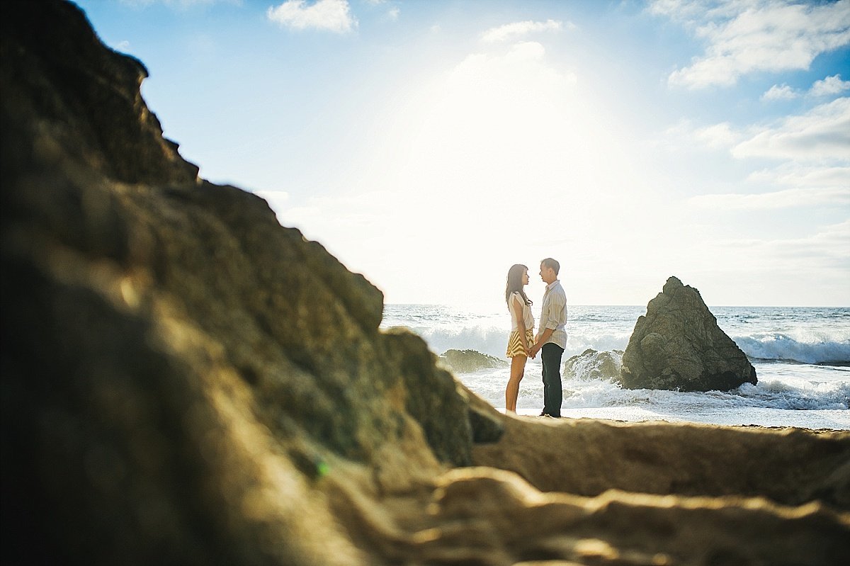 Couple standing in front of rocks along the coast in California