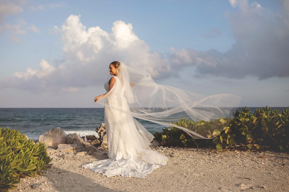 Portrait of a bride from behind as she plays with her veil in the wind at wedding in Riviera Maya