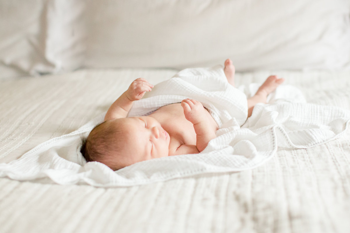 film photography of baby girl laying in white linens of home
