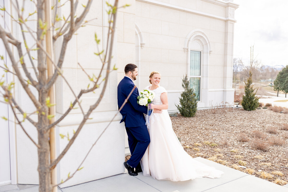 Bride and groom smiling and laughing together near the Taylorsville Utah Temple, creating a joyful candid moment.