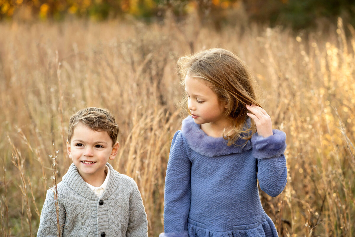 Young girl looking at boy in field while he smiles off camera