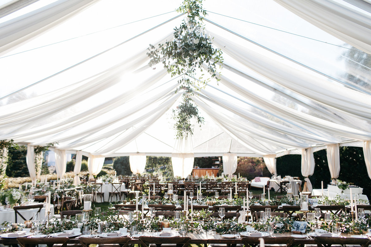 Romantic garden tent wedding with chandeliers covered in greenery and ceiling drapery