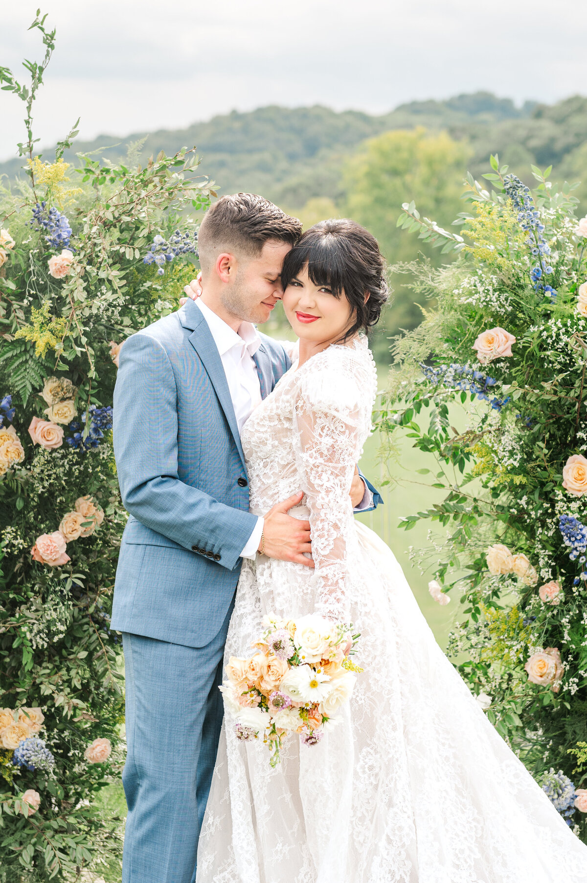 Bride and groom posing in front of floral arch with vibrant colors