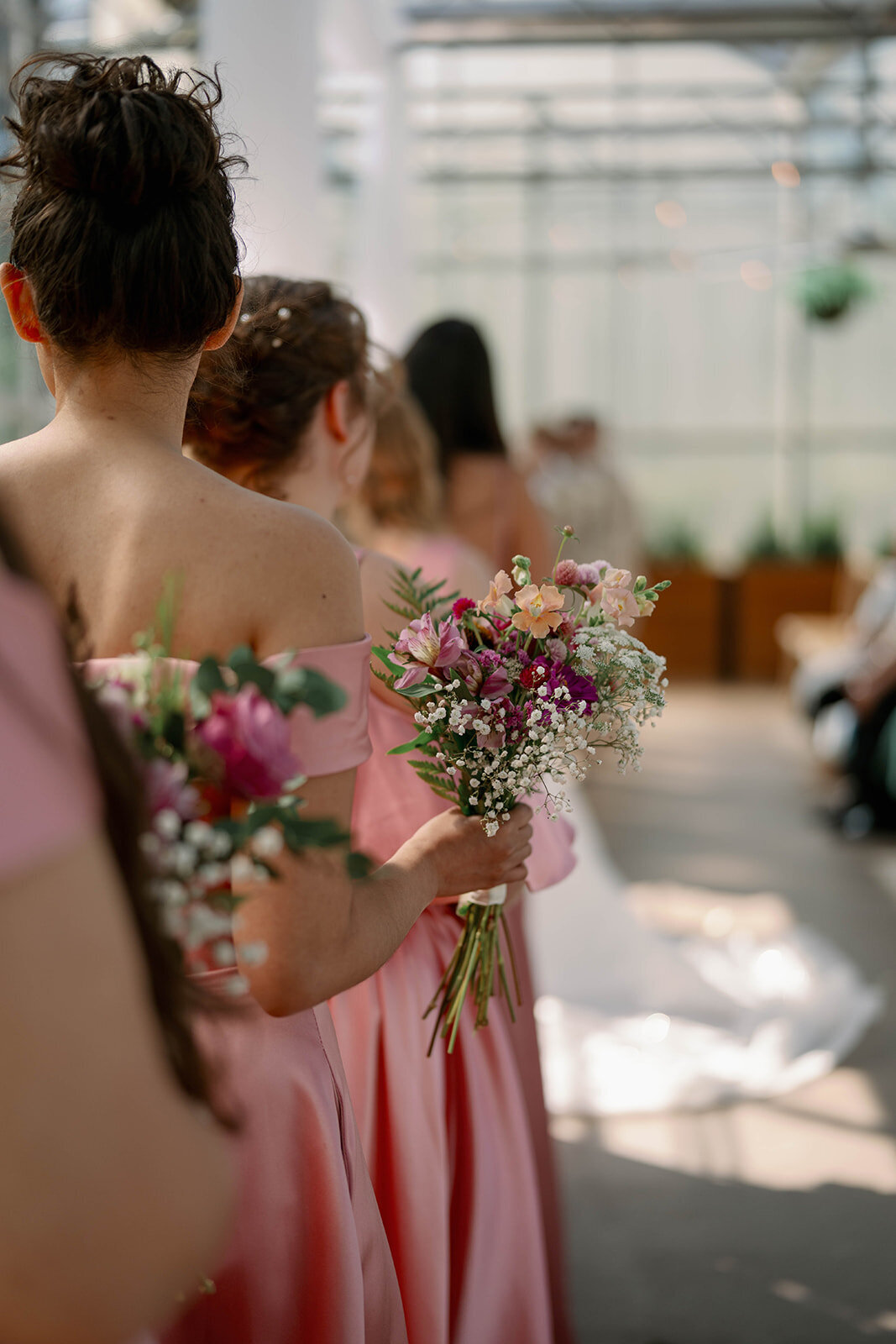Close-up of bridesmaids holding soft, garden-style bouquets during the Ivy House greenhouse wedding ceremony.