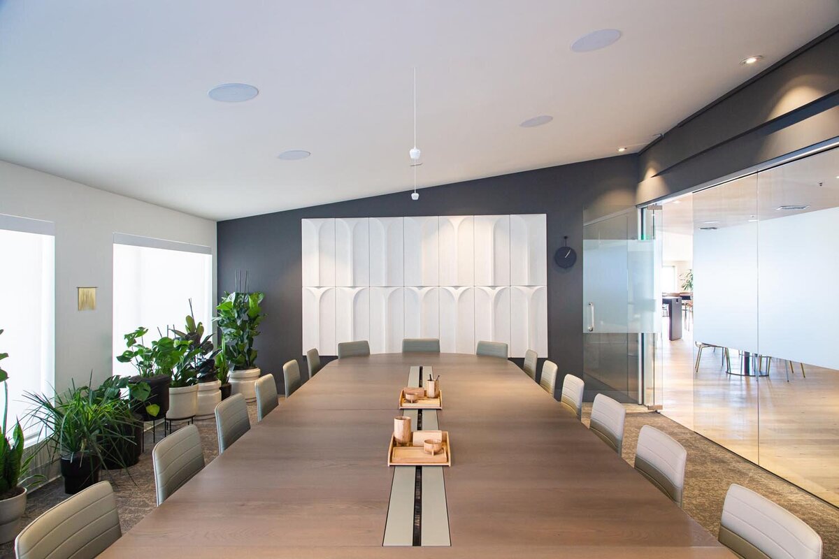 Large modern boardroom with long conference table, plants along the wall, and sculptural white paneling behind the head seats.