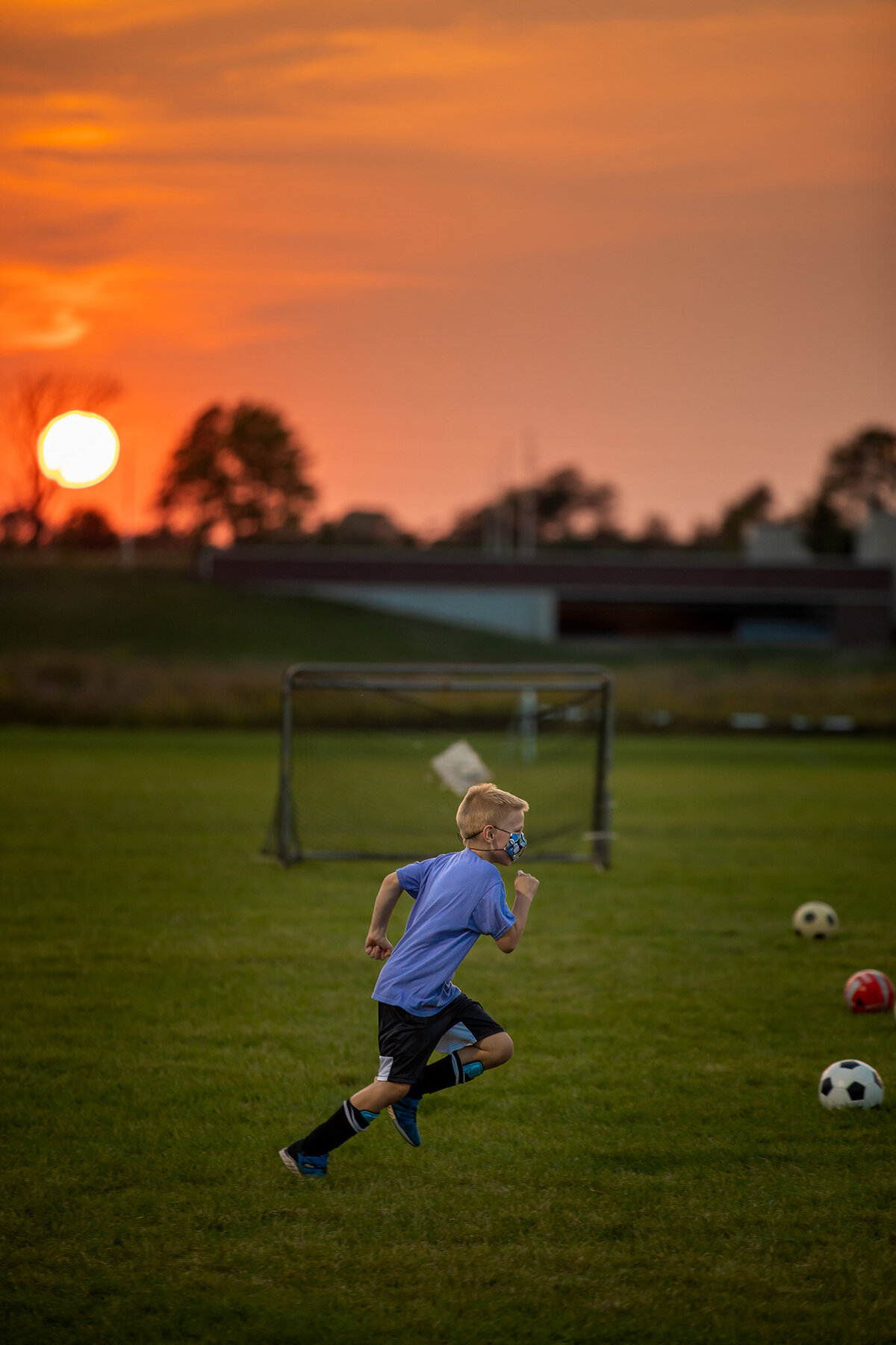boy playing soccer with mask on at sunset
